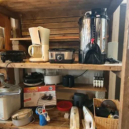 Houten stellingen met huishoudelijke apparaten en keukengerei zoals koffiezetapparaten, mengpannen en andere tweedehands spul