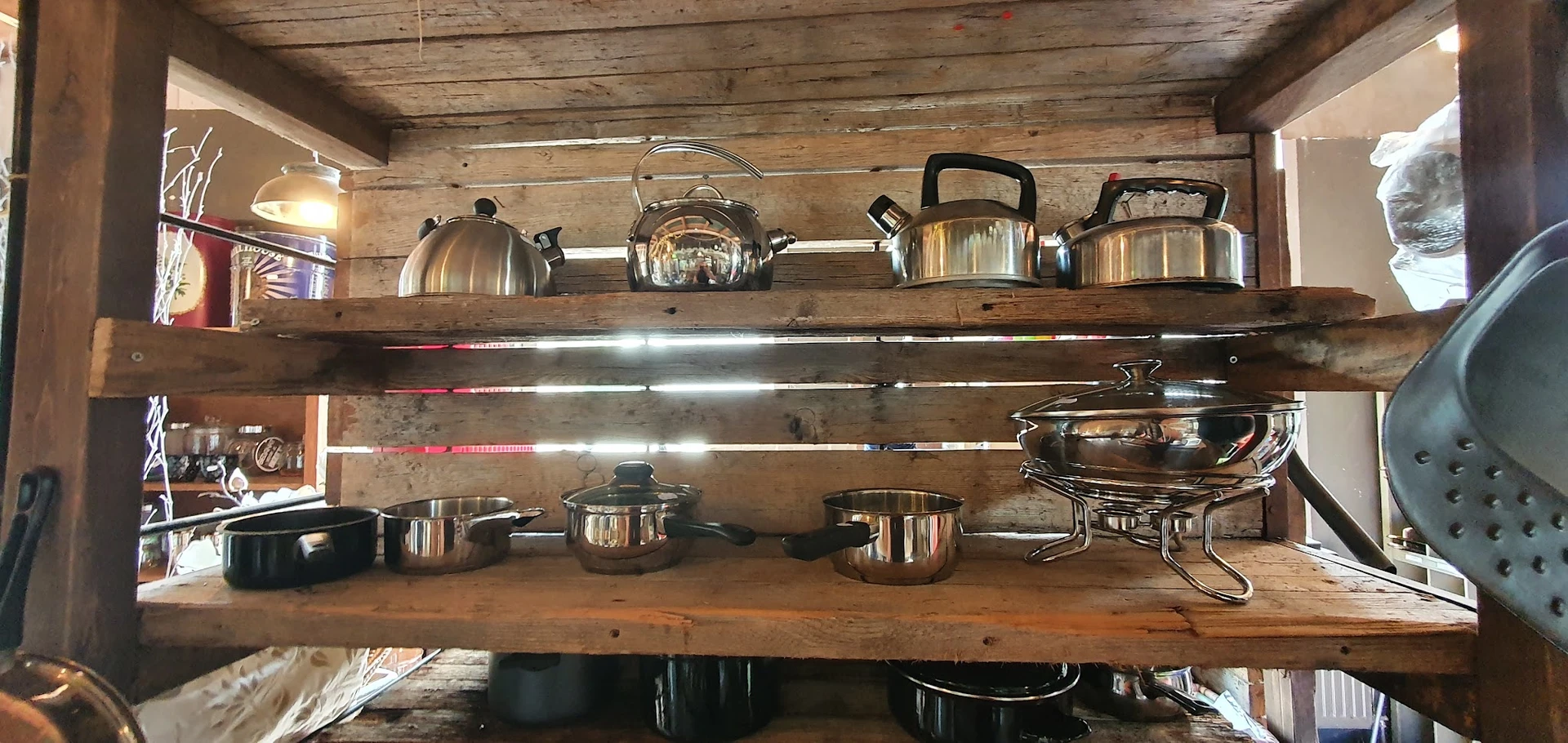 Houten wandrekken met uitgestalde roestvrijstalen keukenpannen, ketels en kookgerei