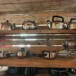Houten wandrekken met uitgestalde roestvrijstalen keukenpannen, ketels en kookgerei