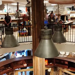 Interieur van kringloopwinkel met hanglampen, zwarte hekwerk, houten balken en bezoekers op verschillende niveaus