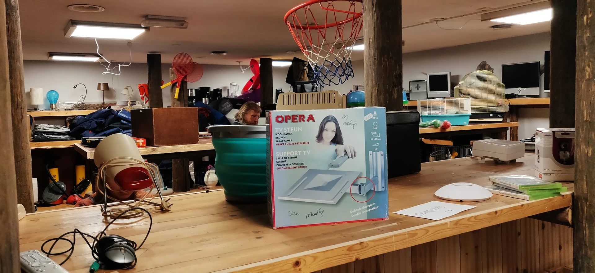 Binnenaanzicht van kringloopwinkel met houten tafel, kartonnen doos, basketbalring en diverse spullen