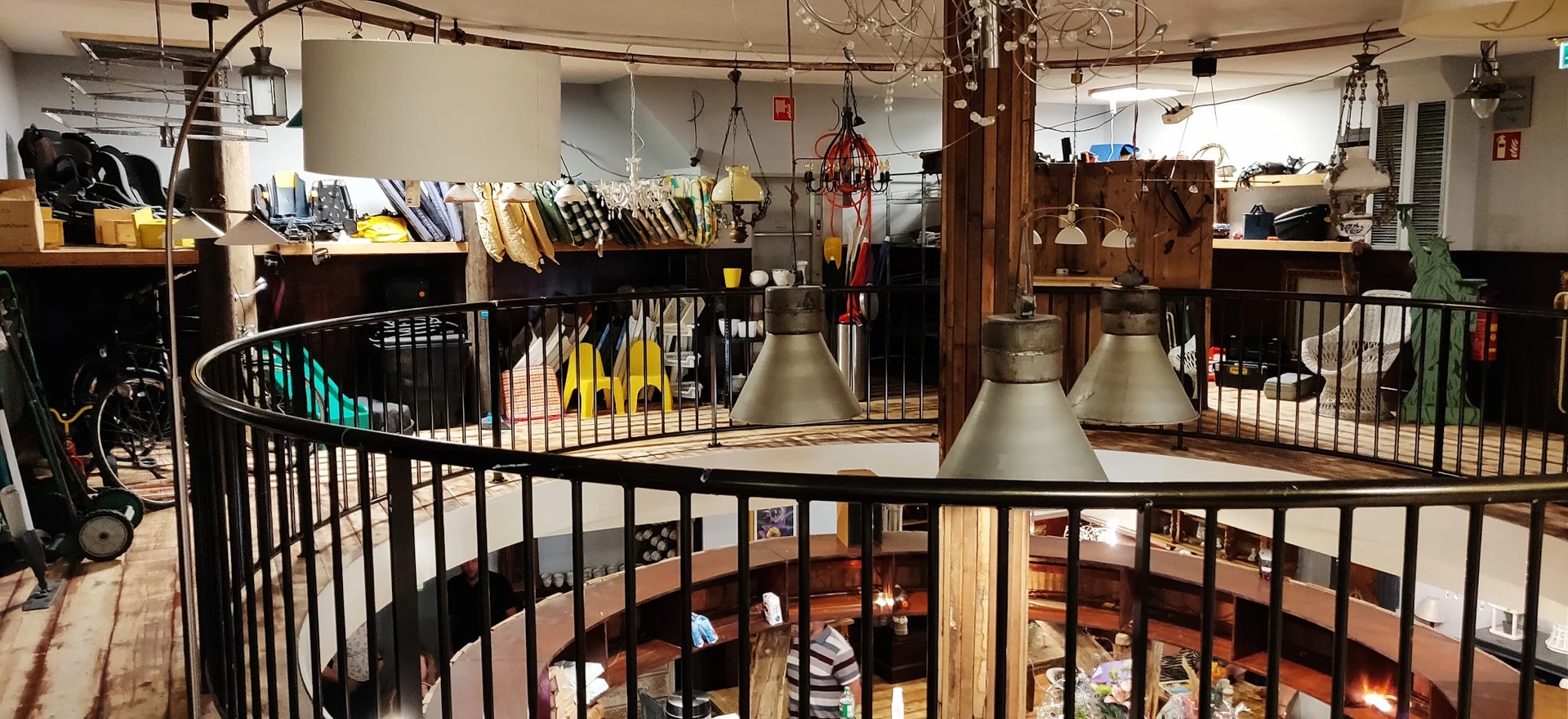 Overzicht van kringloopwinkel met stellingen, hangende lampen, houten meubels en diverse spullen uitgestald