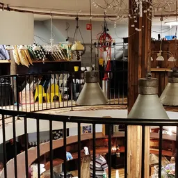 Overzicht van kringloopwinkel met stellingen, hangende lampen, houten meubels en diverse spullen uitgestald