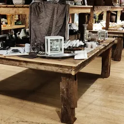 Houten tafel met diverse items zoals witte decoraties, een glazen kast en huishoudelijke spullen in een kringloopwinkel