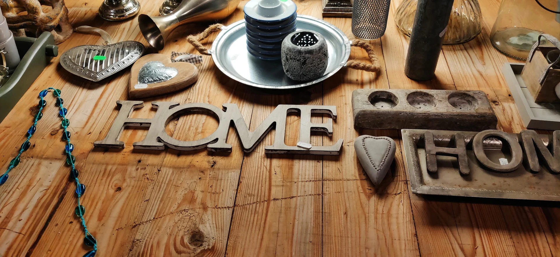 Huishoudelijke decoratieartikelen en speelgoed uitgestald op houten tafel, waaronder het woord HOME en diverse keukengereedsc