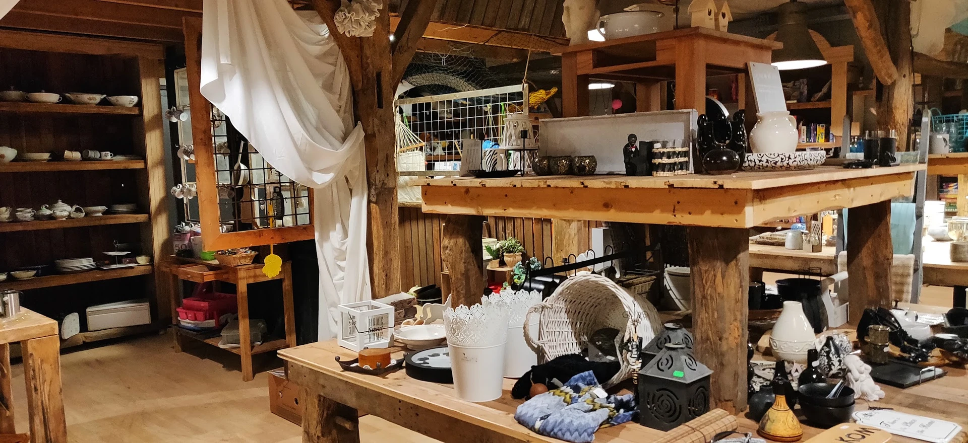 Houten stellingen en tafels vol met tweedehands spullen, huishoudartikelen en textiel in een kringloopwinkel