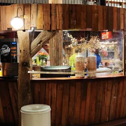 Koffiehoek met houten bar, koffiemachine en display met bloemen in kringloopwinkel