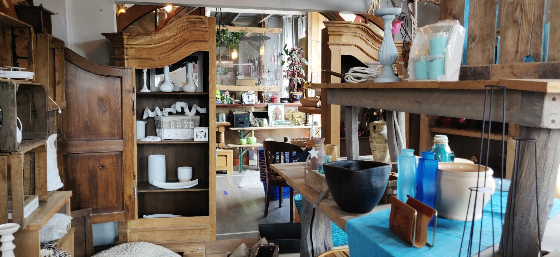 Winkelbinnenruimte met houten kastjes, planken met huishoudartikelen, decoratieve items en een zwarte kom op de toonbank