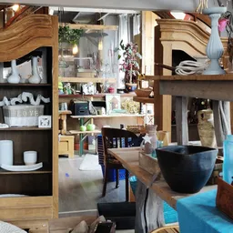 Winkelbinnenruimte met houten kastjes, planken met huishoudartikelen, decoratieve items en een zwarte kom op de toonbank