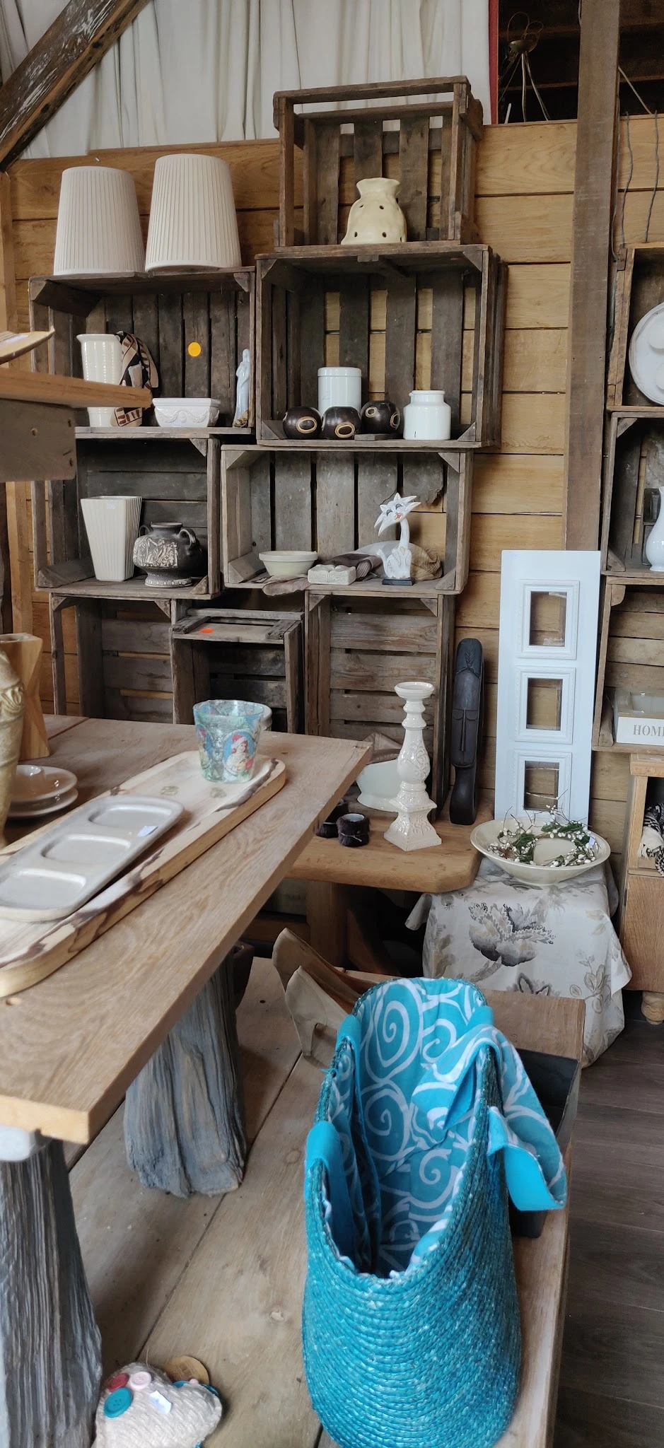 Houten tafel met diverse huishoudartikelen en decoratieve items, tegen achtergrond met houten kisten en stellingen vol spulle