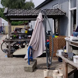 Buitenterrein met parasol, fiets, diverse spullen en houten schuur