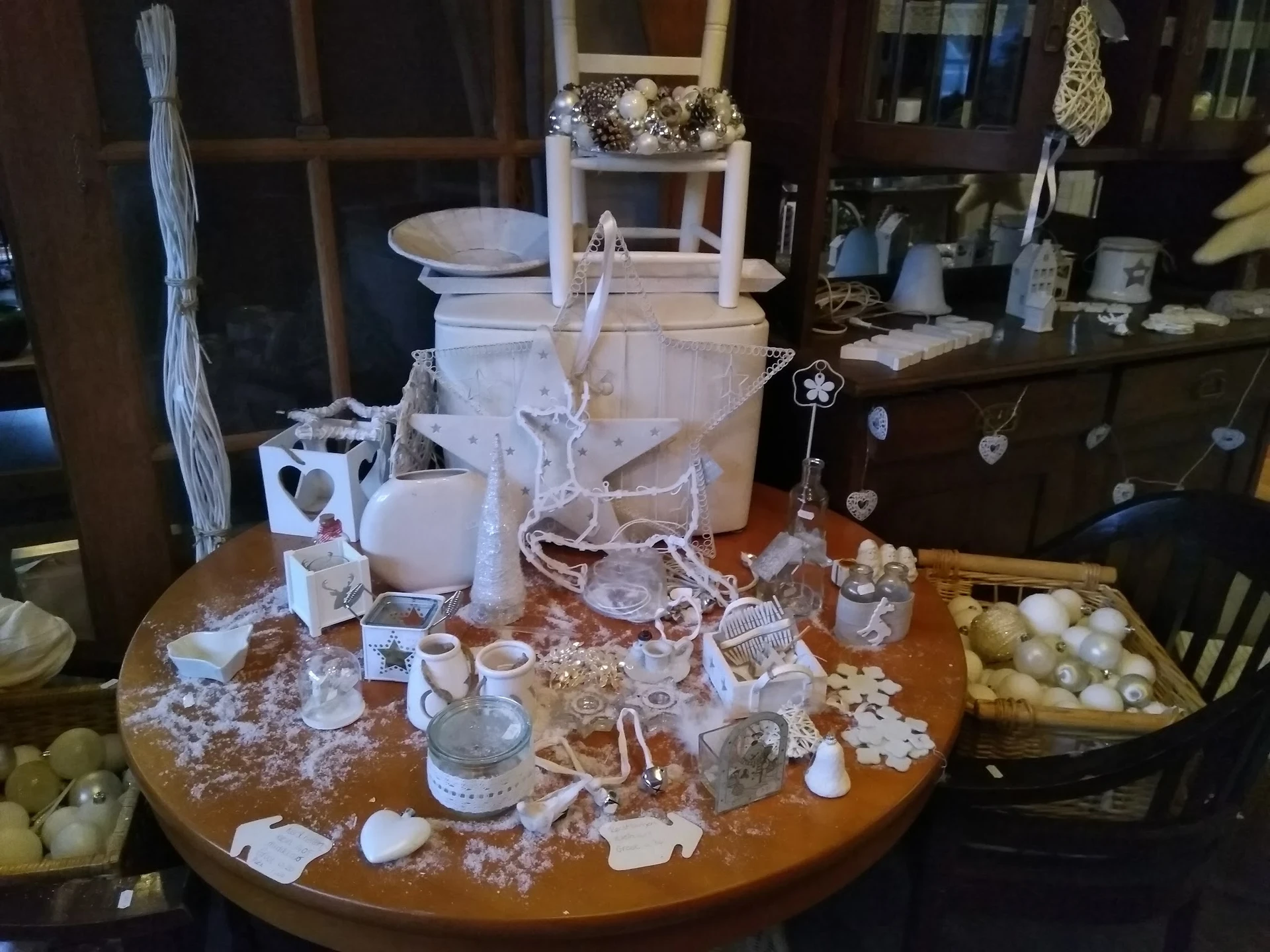 Ronde tafel vol witte decoratieve artikelen, kaarsen, vazen en huishoudartikelen in een kringloopwinkel