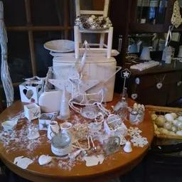 Ronde tafel vol witte decoratieve artikelen, kaarsen, vazen en huishoudartikelen in een kringloopwinkel