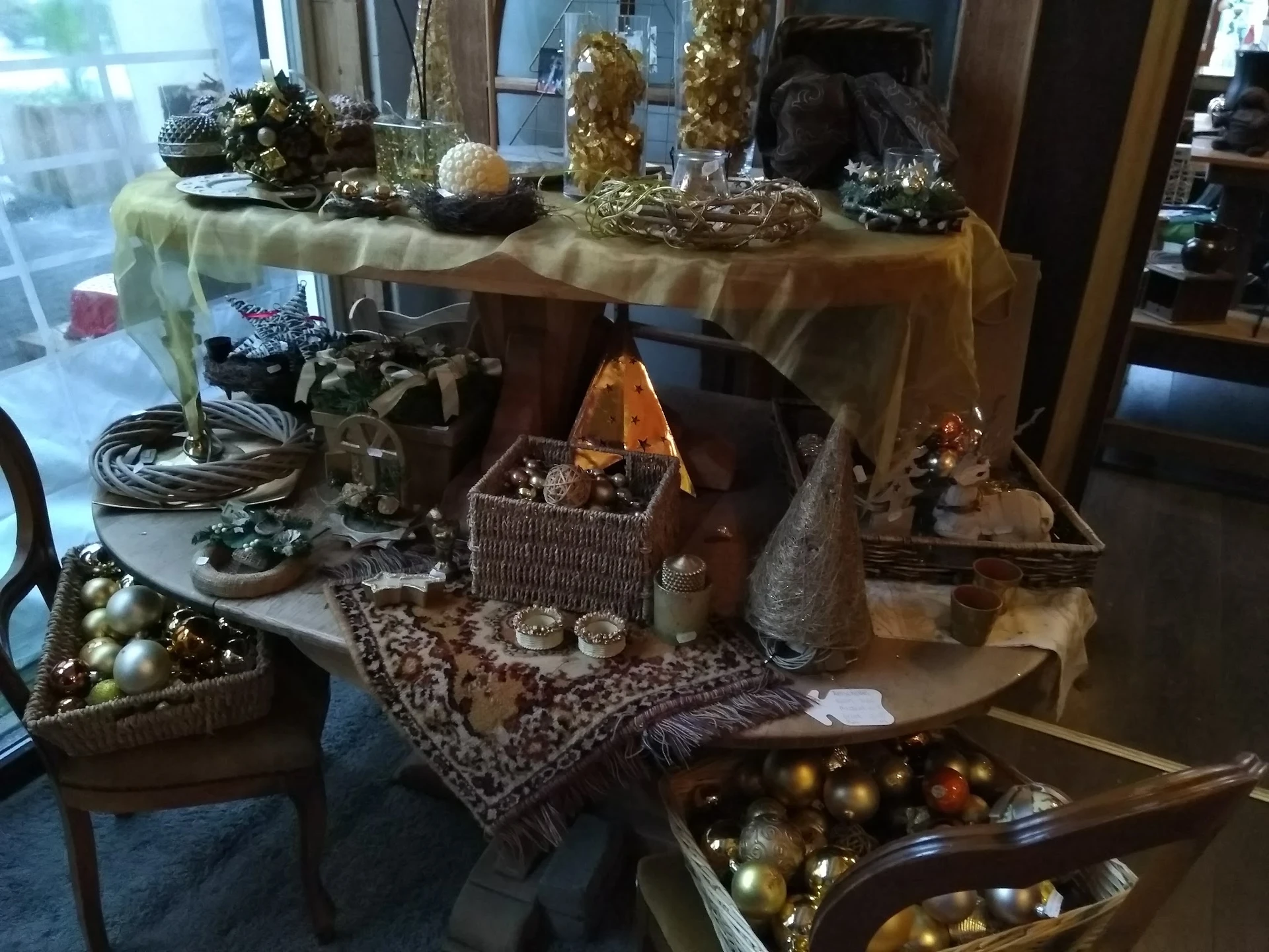 Kerstdecoratie en versieringen uitgestald op tafels, met gouden en zilveren ballen, takken in vazen en feestelijke ornamenten