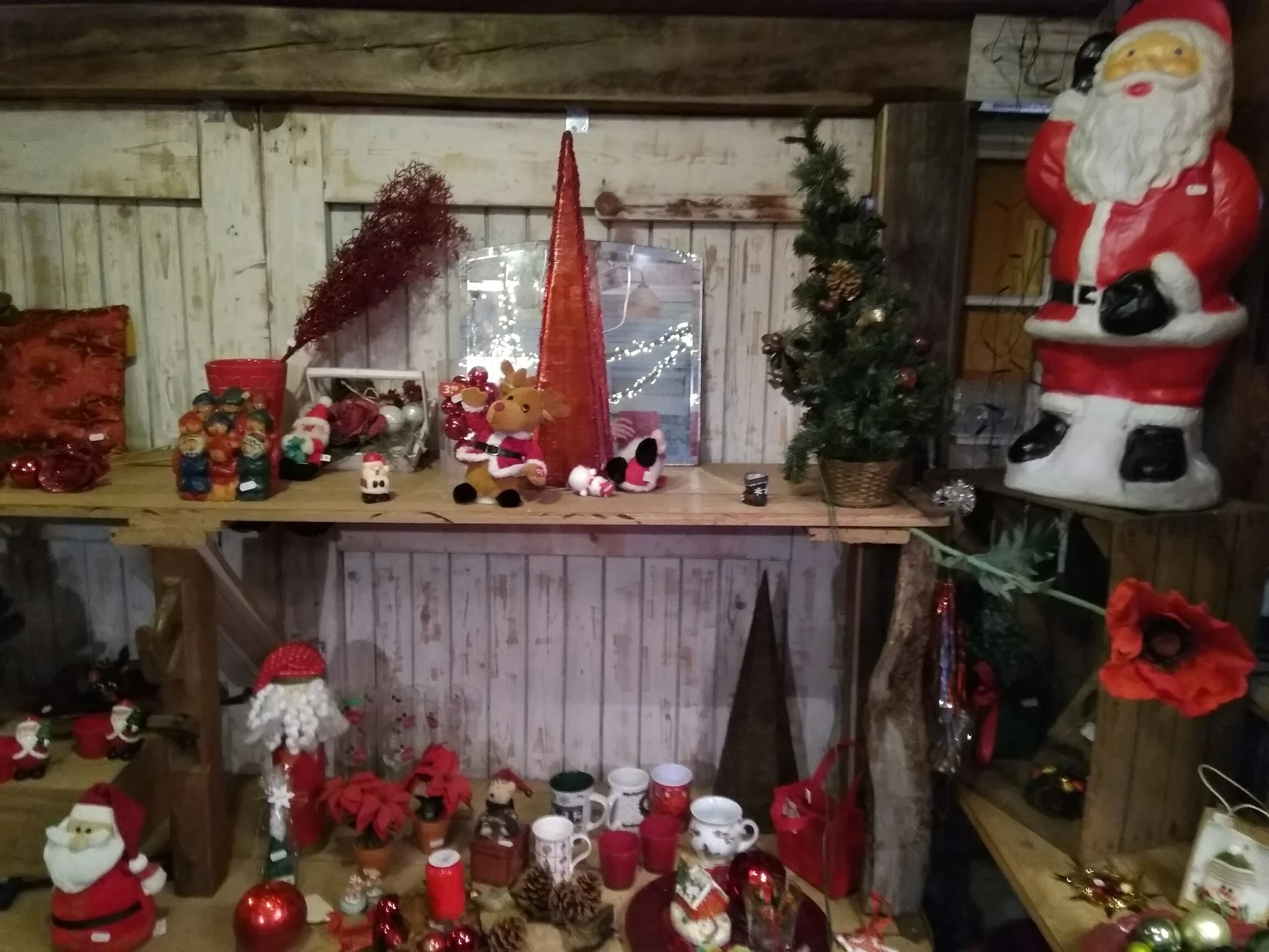 Kerstdecoratie en kerstversiering uitgestald op schappen en meubels, met kaarsen, beelden en rode kerstkransen
