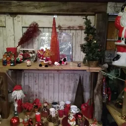Kerstdecoratie en kerstversiering uitgestald op schappen en meubels, met kaarsen, beelden en rode kerstkransen