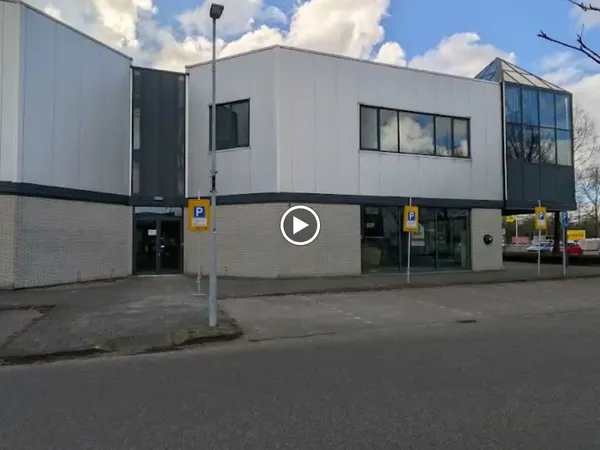 Moderne gevel van kringloopwinkel met witte en grijze gevelbekleding, ingang met deuren en parkeerplaatsen ervoor