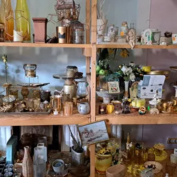 Houten stellingen volgesteld met diverse huishoudelijke artikelen, kandelaars, flessen, serviesgoed en decoratieve voorwerpen
