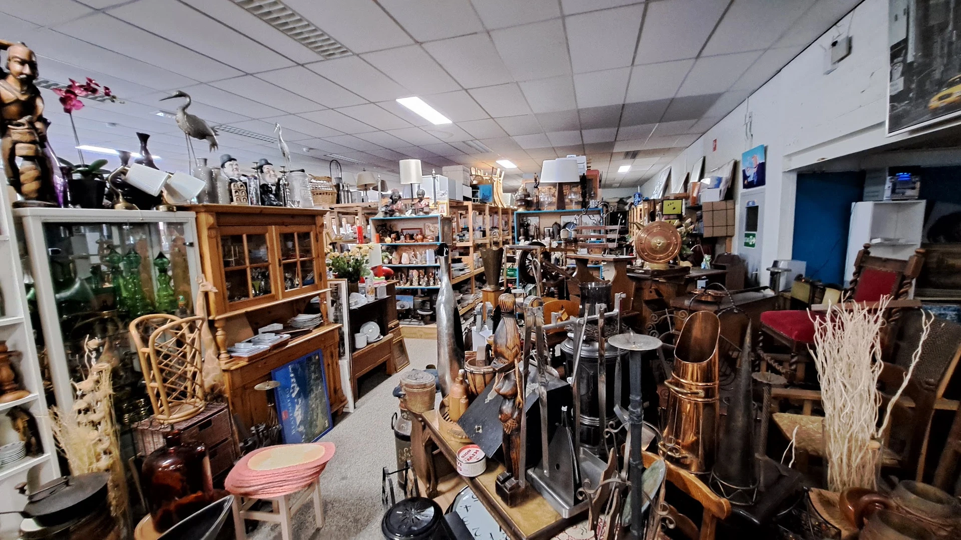 Overzicht van de winkelvloer met diverse tweedehands spullen, meubilair, muziekinstrumenten en huishoudartikelen op stellinge