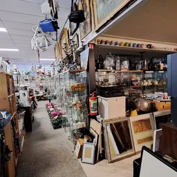 Winkelvloer van kringloopwinkel met stellingen, diverse koopwaar, hanglampen en kasten met spullen