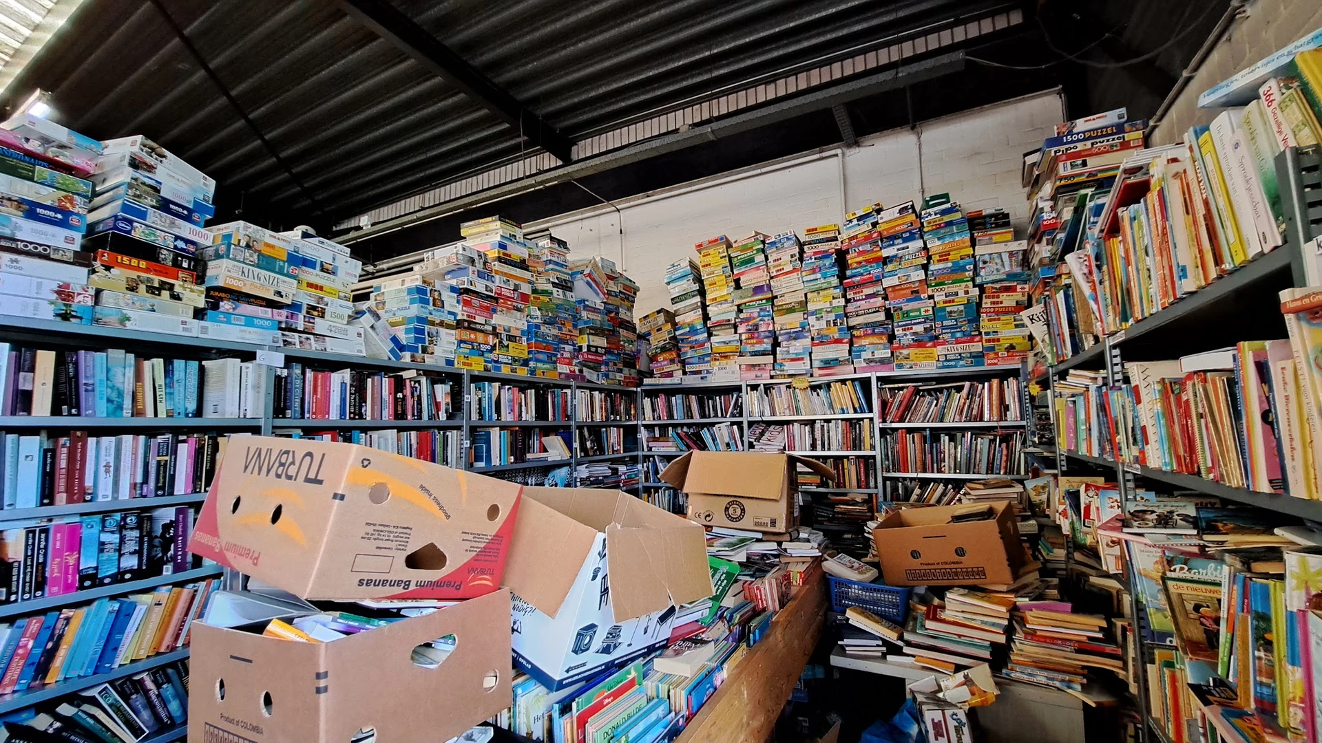 Magazijnruimte met hoge stellingen vol boeken, dvd's en dozen in een kringloopwinkel