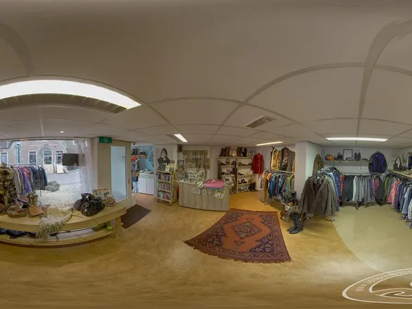 Winkelvloer van kringloopwinkel met kledingrekken, kasten, decoratief tapijt en sfeervolle verlichting aan het plafond