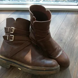 Paar bruine laarzen met gesp, uitgestald op houten vloer