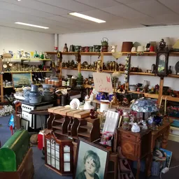 Overzicht van de winkelruimte met houten stellingen vol spullen, tafels met diverse voorwerpen en huishoudartikelen.