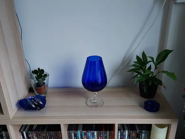 Blauwe glazen vaas op voet, tussen potplanten op houten kastrek