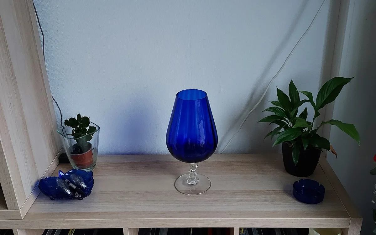 Blauwe glazen vaas op voet, tussen potplanten op houten kastrek