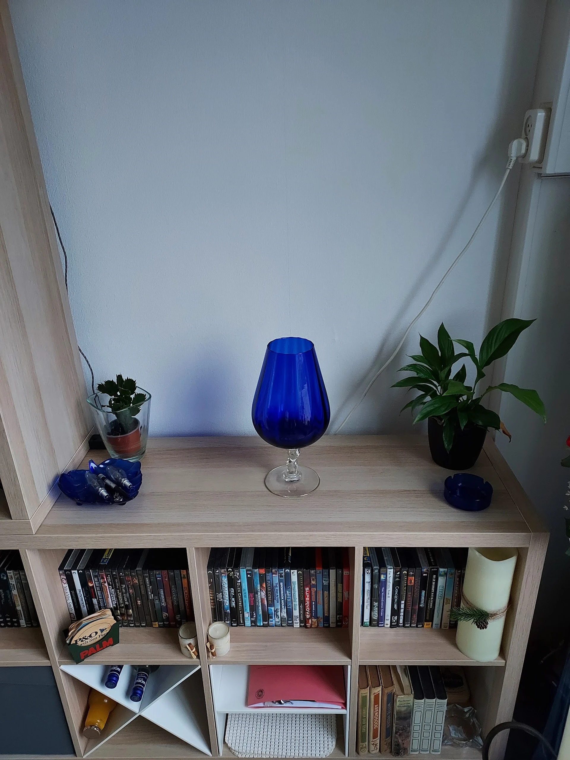 Blauwe glazen vaas op voet, tussen potplanten op houten kastrek