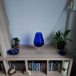 Blauwe glazen vaas op voet, tussen potplanten op houten kastrek
