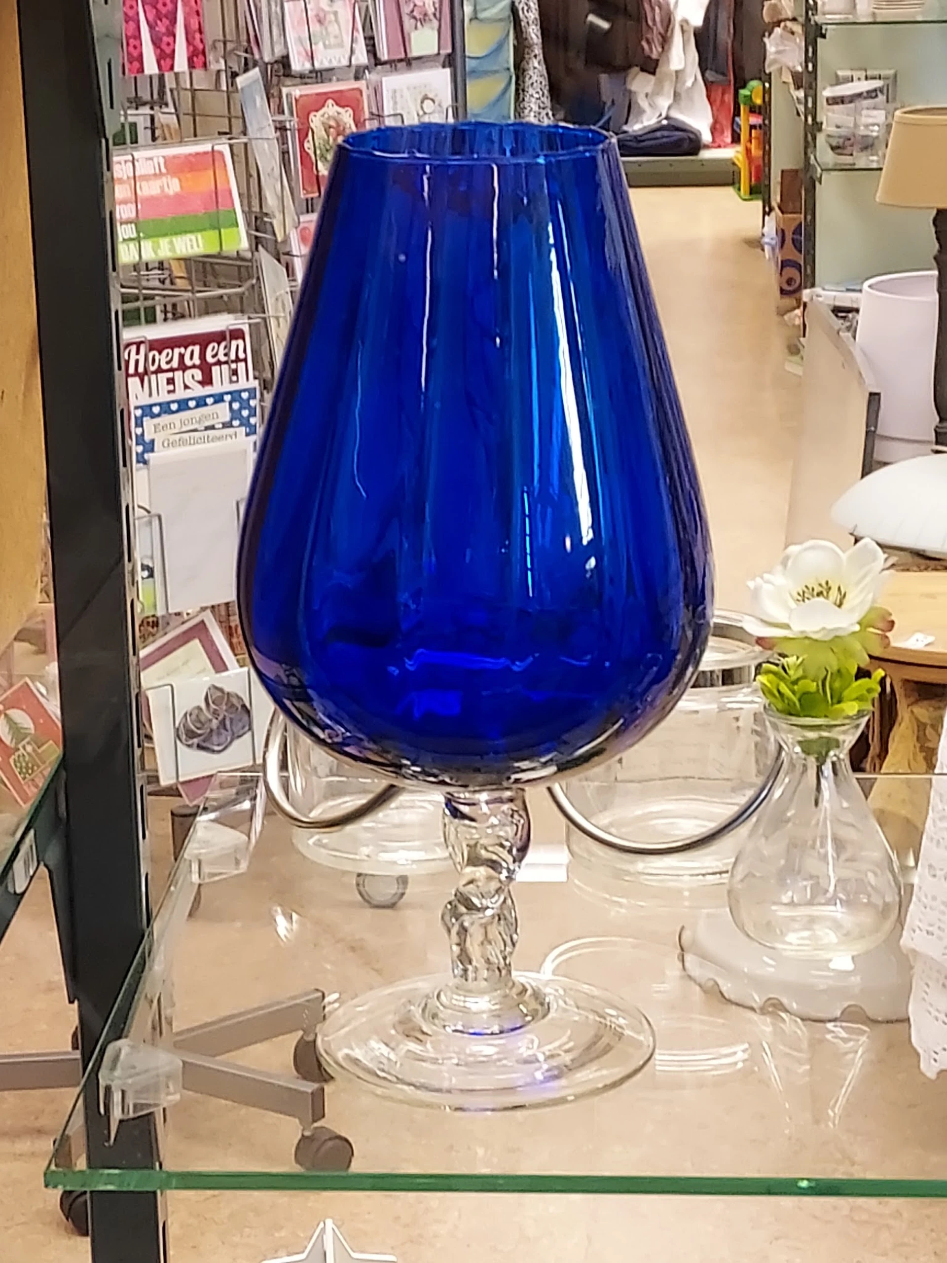 Blauwe glazen vaas met druppelvorm op glazen voet met andere glazen items op achtergrond