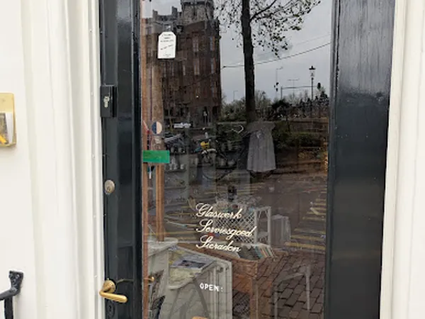 Glazen deur van kringloopwinkel met uitzicht op straat en gebouwen, gedeeltelijk bedekt door condensatie