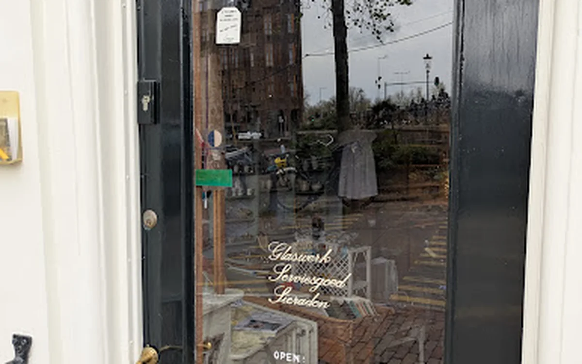 Glazen deur van kringloopwinkel met uitzicht op straat en gebouwen, gedeeltelijk bedekt door condensatie