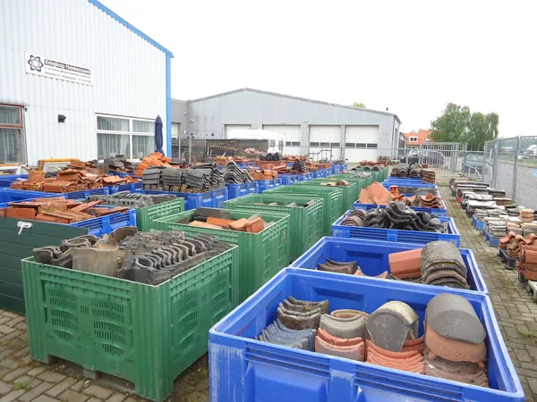 Groene en blauwe kunststofbakken buiten met diverse gebruikte items zoals servies, keramiek en bouwmaterialen