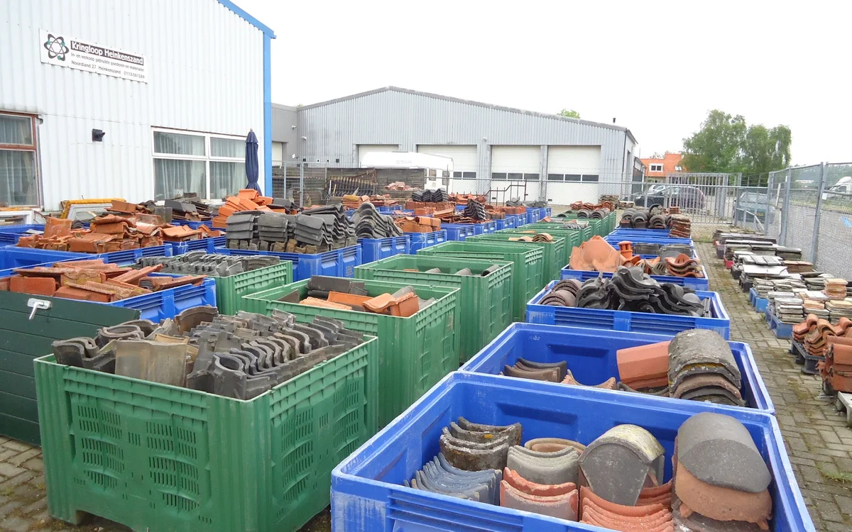 Blauwe en groene plastic bakken vol met gebruikt bouwmateriaal en onderdelen op een sloopwerkenterrein