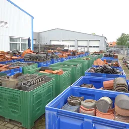 Groene en blauwe kunststofbakken buiten met diverse gebruikte items zoals servies, keramiek en bouwmaterialen