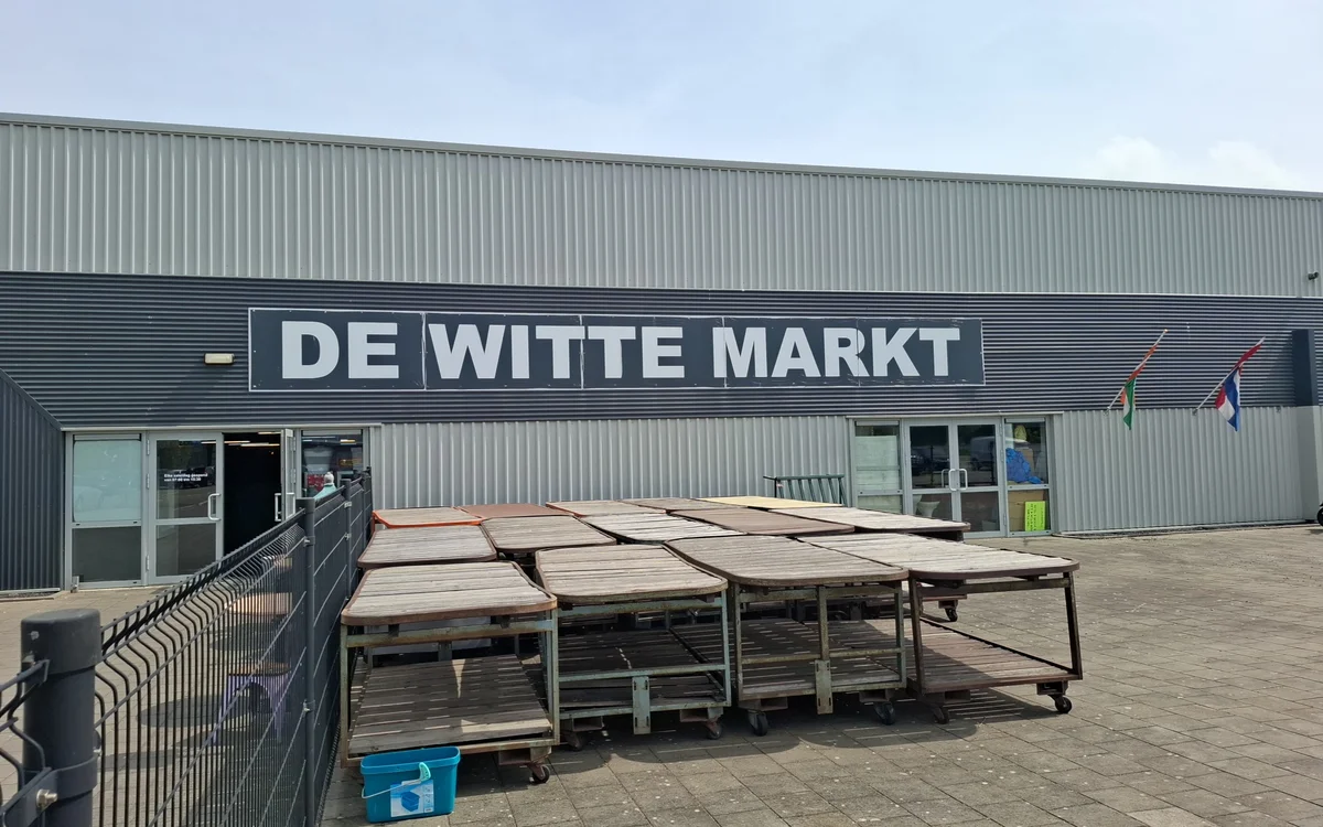 Gevel van kringloopwinkel De Witte Markt met naambord, ingang en terras met tafels ervoor