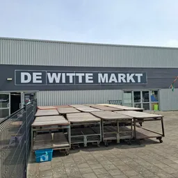 Gevel van kringloopwinkel De Witte Markt met naambord, ingang en terras met tafels ervoor