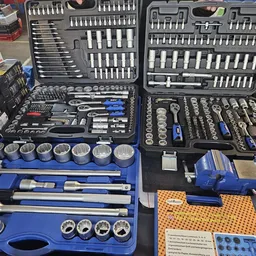 Uitgestalde gereedschapssets en sokkelsets met doppen, sleutels en bits in blauwe opbergkoffers