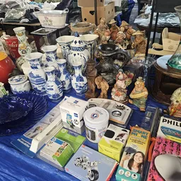 Uiteenlopend aanbod van gebruikte artikelen: blauw servies, beeldjes, huishoudapparaten en decoratie op blauwe ondergrond.