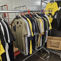 Rekken met tweedehands kleding in geel, zwart, wit en beige tinten, met ELEVON-doos op kar