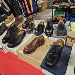 Uitgestalde herenschoenen en laarzen op tafels met dozen, in de achtergrond kleding op hangers