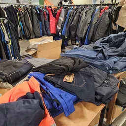Uitgestalde tweedehands kleding op tafels en aan kledingrekken in de winkel
