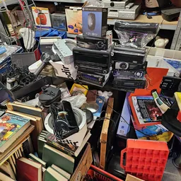 Chaotisch assortiment van elektronica, speelgoed, boeken en huishoudartikelen op tafels en stellingen