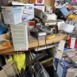 Rommelige tafel met elektronische apparaten, lamineerapparaten, foto's en verschillende items door elkaar