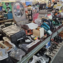 Tafel vol met diverse tweedehands huishoudelijke apparaten en elektronica zoals een koffiemachine, gereedschap en andere item