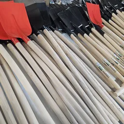 Rijen spaden met houten en kunststof handvatten in verschillende kleuren, uitgestald op een rek