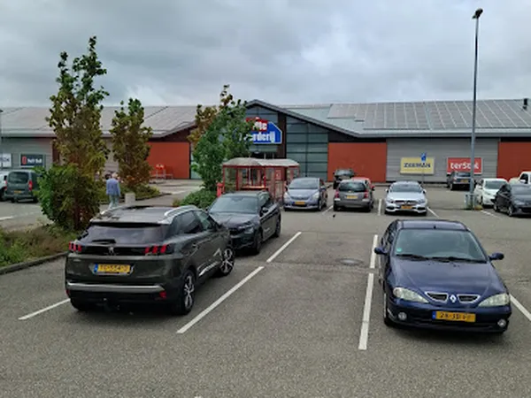 Parkeerplaats met auto's voor de rode gevel van kringloopwinkel De Witte Markt